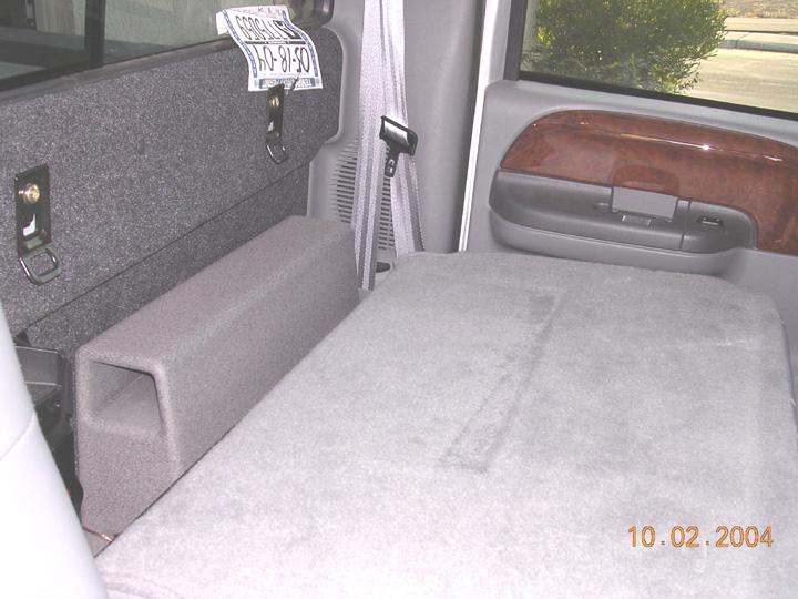 Rear cab interior of pickup with folded gray seat, carpeted box against back wall, and paper temp tag