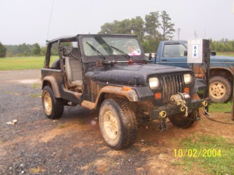 1994 Jeep YJ - A muddy Jeep Wrangler is parked next to a blue pickup truck, with an air pump station nearby.