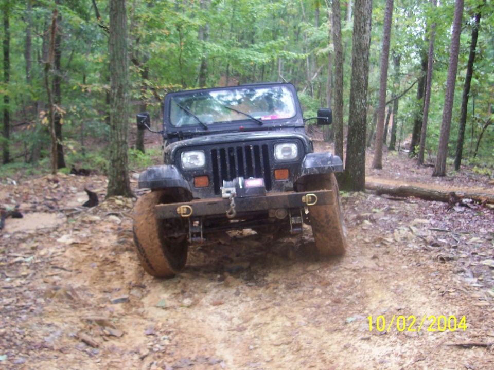 Black 1994 Jeep YJ on a muddy forest trail, front view