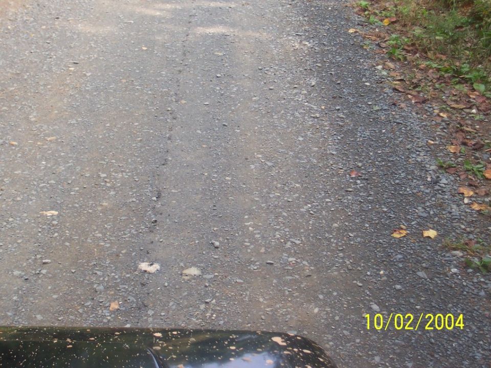 Gravel road with a dark vehicle fender in the foreground. Date stamp reads 10/02/2004