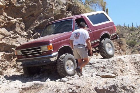 1990 Ford Bronco - 1990 Ford Bronco tackling a challenging off-road trail in a desert landscape.