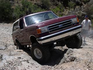 1990 Ford Bronco - This Ford Bronco is navigating a rocky, off-road trail with a person observing the action.