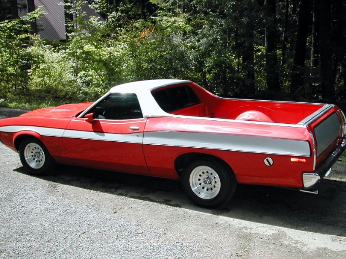 Red and white Ford Ranchero pickup, rear three-quarter view, parked on gravel road by woods
