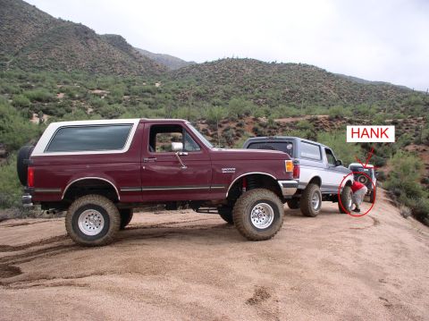 1990 Ford Bronco - Two Ford Broncos on a trail, one with a man attending to a tire.