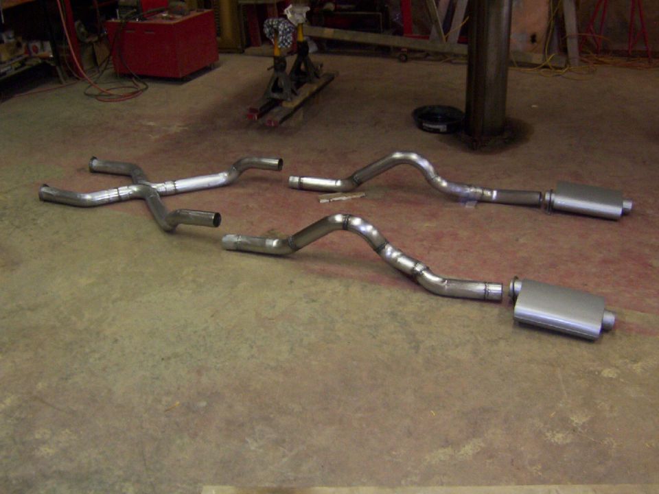 Dual exhaust system with mufflers and a crossover pipe laid out on a concrete floor
