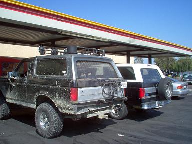 1988 Ford Bronco - Two SUVs are parked side-by-side under an outdoor canopy on a sunny day.