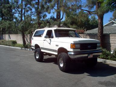 1988 Ford Bronco - A white Ford Bronco is parked outdoors on a paved surface with trees and a building visible.