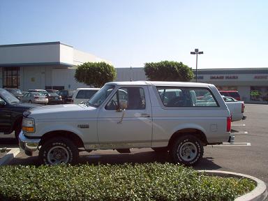1988 Ford Bronco - A silver Ford Bronco is parked in a lot with a building in the background.