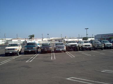 1988 Ford Bronco - Multiple Ford trucks and SUVs are parked in a lot on a sunny day.