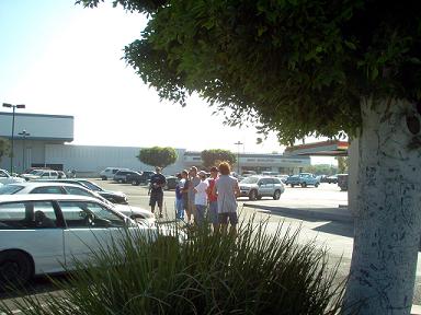 1988 Ford Bronco - A group of people stand in a parking lot near several vehicles, with a building and gas station in the background.