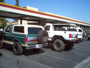 1988 Ford Bronco - Two SUVs are parked under a covered structure on a sunny day.