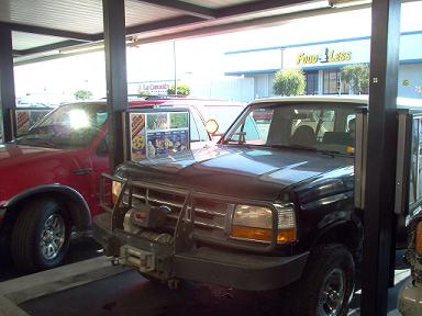 1988 Ford Bronco - Two trucks are parked under a covered area, possibly a drive-thru or parking garage.