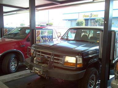 1988 Ford Bronco - A black Ford Bronco is parked next to a red pickup truck under a covered area.