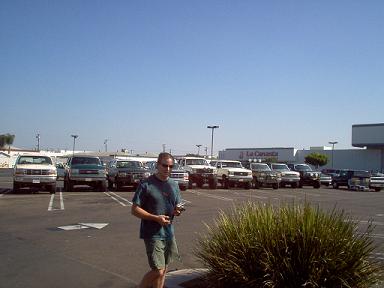 1988 Ford Bronco - A group of off-road vehicles, primarily Ford Broncos, are gathered in a parking lot on a sunny day.