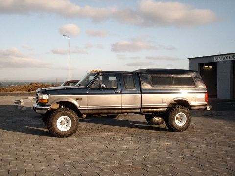 1996 Ford Bronco - A lifted Ford F-250 pickup truck with a camper shell is parked on a paved lot near the ocean.