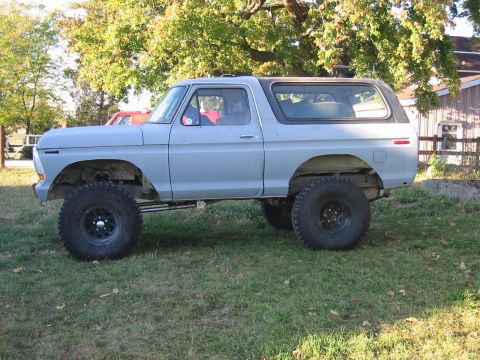 1992 Ford Bronco - This light blue SUV, likely a 1978 Ford Bronco, is shown from the side with oversized tires and a grey hardtop.