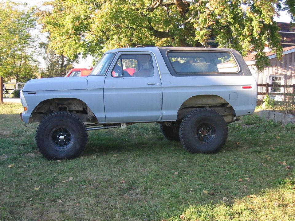 Light blue SUV with large tires parked on grass, side view. Appears to be a 1978 Ford Bronco