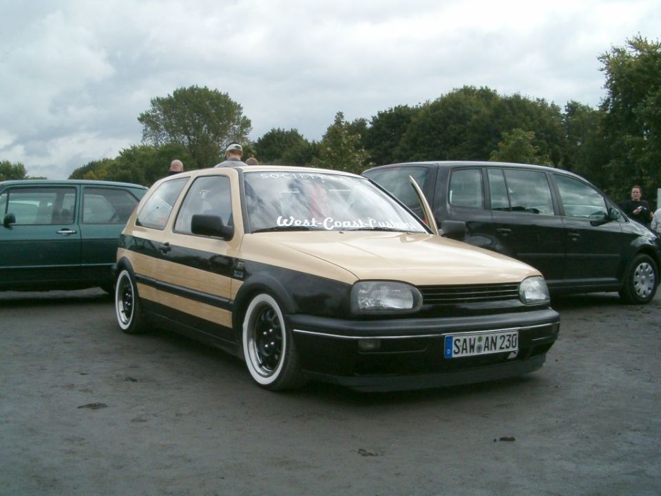 Tan and black VW Golf Mk3 with whitewall tires and a sticker on the windshield