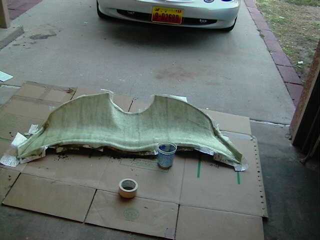 Fiberglass car stereo component on cardboard with tape and a cup. Car bumper visible in background