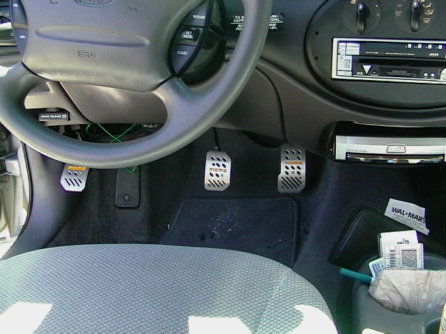Car interior showing a steering wheel, dashboard, and custom MOMO pedals. A Wal-Mart receipt is visible