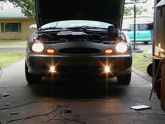 1999 Ford Taurus front view, hood open, showing engine bay and headlights on