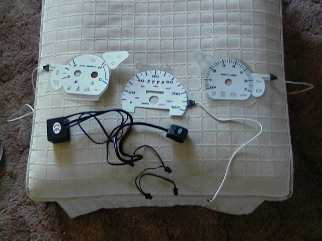 Three white gauge faces with black markings and wires. One has a fuel gauge