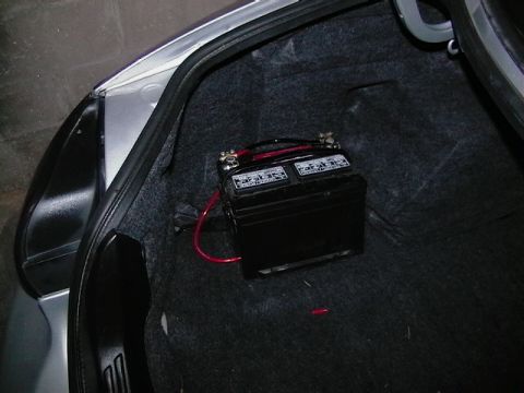 1999 Ford Taurus - A car battery is installed in the trunk of a vehicle, with red cables connected.