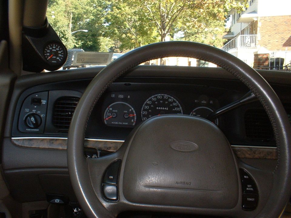 Tan interior of a Ford sedan with steering wheel, gauge cluster, and A-pillar mounted VDO tachometer pod