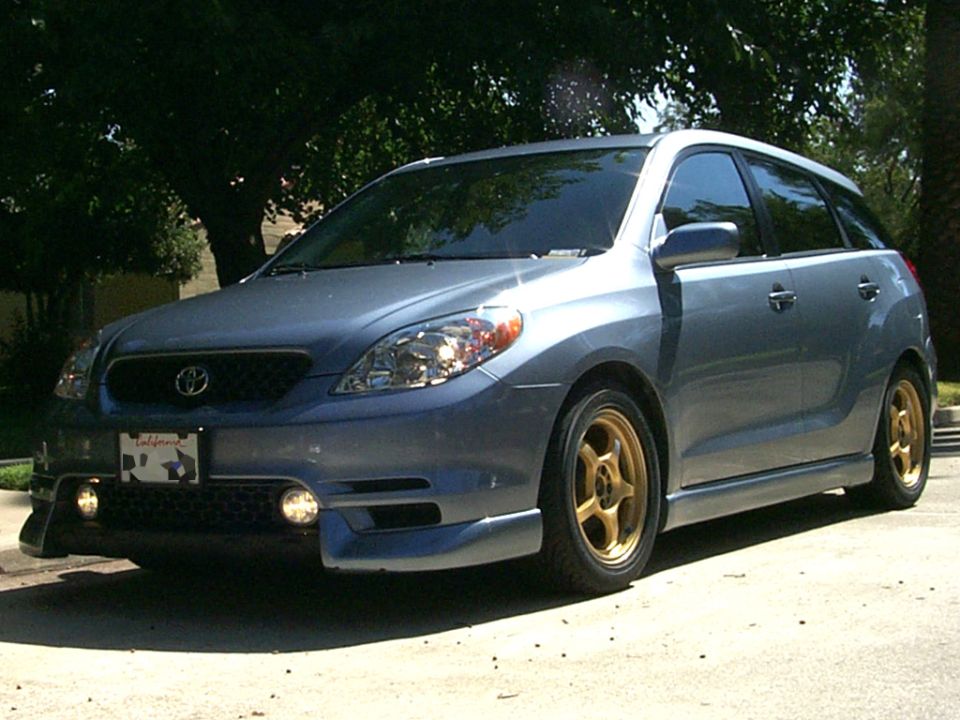 Steel-blue Toyota Matrix with gold aftermarket wheels and front lip kit parked under trees