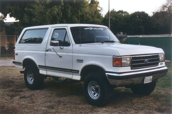 White Ford Bronco 4x4 SUV, front three-quarter view, lifted on off-road tires, parked on grass