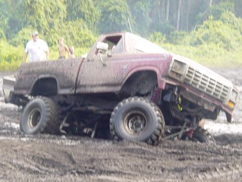 1989 Ford Bronco - Muddy pickup truck with lifted suspension and large tires is stuck in a muddy field.