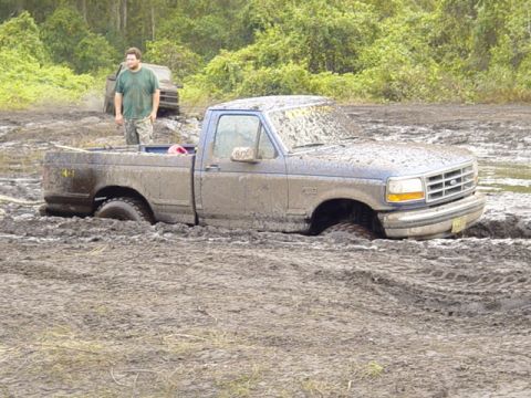 1989 Ford Bronco - A 1992 Ford F-150 is stuck deep in the mud, with a man observing from the side.