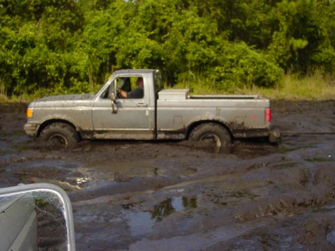 1989 Ford Bronco - Silver Ford pickup truck is stuck in mud, with trees visible behind it.
