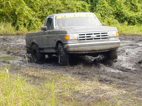 1989 Ford Bronco - A muddy Ford F-Series truck navigates through a challenging off-road mud pit.