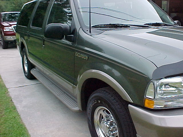 Green Ford Excursion with running boards and a red Ford F-150 behind it