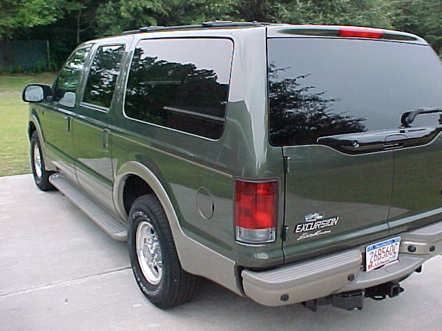 Green 2003 Ford Excursion rear quarter view with tinted windows and a trailer hitch