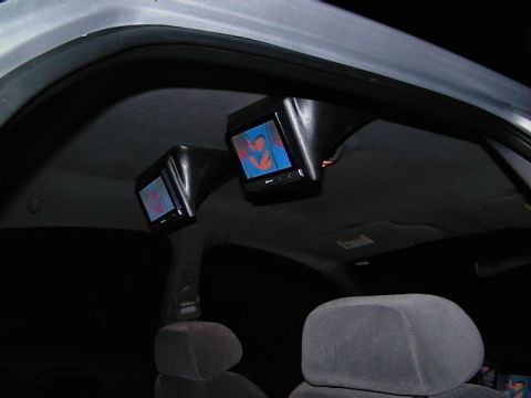 1999 Ford Taurus - Aftermarket screens are mounted to the car's interior ceiling, displaying video content.