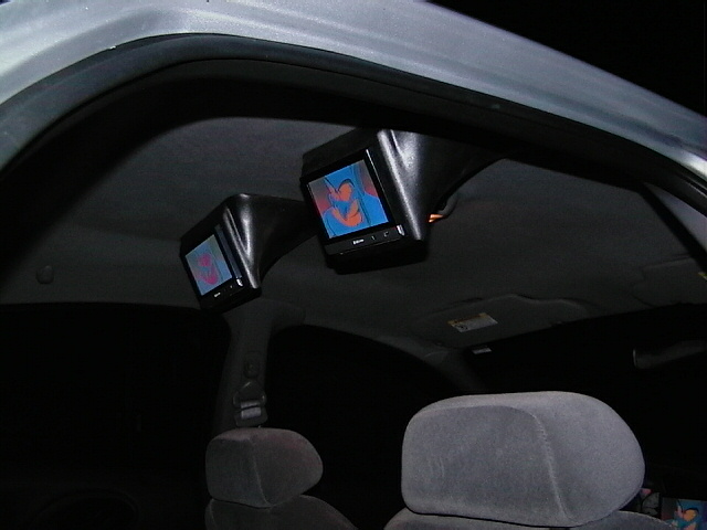 Interior view of car with two aftermarket screens mounted overhead, showing colorful images