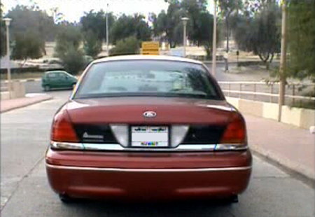 2000 Ford Crown Victoria - Rear view of a red 2000 Ford Crown Victoria parked on a street with a green car in the background.