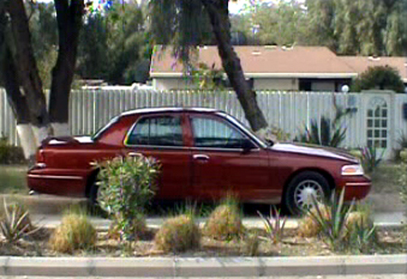 2000 Ford Crown Victoria - Side profile of a red 2000 Ford Crown Victoria parked in front of a house and fence.