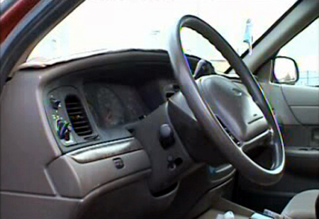 2000 Ford Crown Victoria - The interior of a car shows the dashboard, steering wheel, and driver's side door panel.
