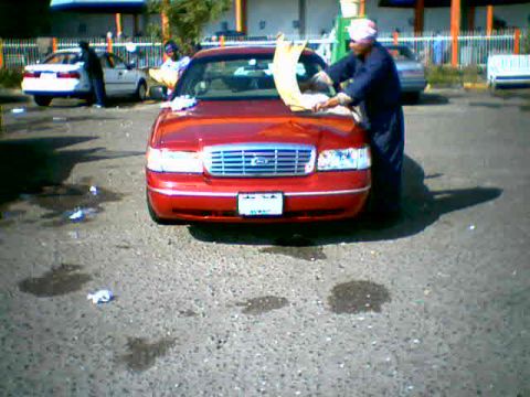 2000 Ford Crown Victoria - A red 2000 Ford Crown Victoria is being washed in a parking lot, with another white car visible in the background.