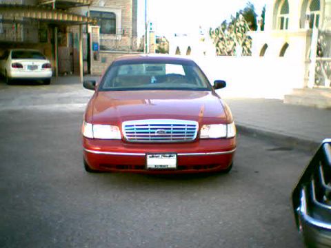 2000 Ford Crown Victoria - A red 2000 Ford Crown Victoria is seen from the front, with another white car parked behind it.