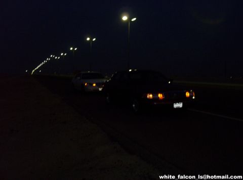 2000 Ford Crown Victoria - Two Ford Crown Victorias drive down a dark road at night, illuminated by streetlights.