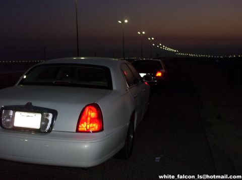 2000 Ford Crown Victoria - Two cars drive down a road at dusk, illuminated by streetlights.