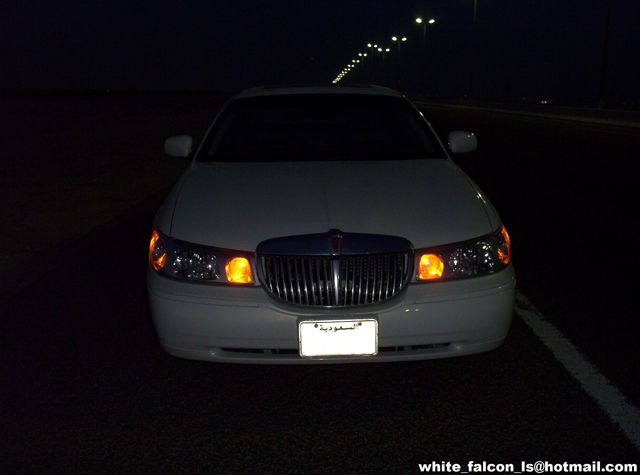 White sedan with chrome grille and amber turn signals, front view at night
