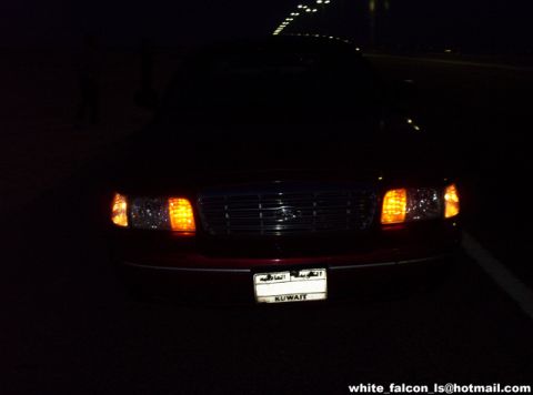 2000 Ford Crown Victoria - The front of a red sedan is visible at night, its headlights and grille.
