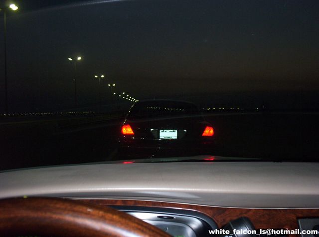 Car driving on a dark road at night, with streetlights in the distance. The taillights of the car ahead are visible