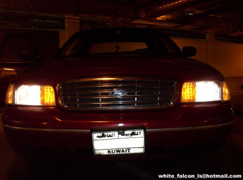 2000 Ford Crown Victoria - A red Ford Crown Victoria is seen from the front, with its headlights illuminated.