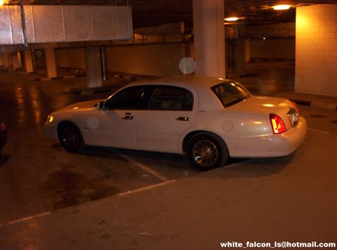 2000 Ford Crown Victoria - A white sedan is parked in a dimly lit garage. The vehicle's side profile is visible.
